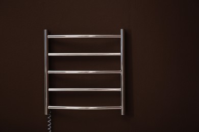 Modern heated towel rail on brown wall. Space for text