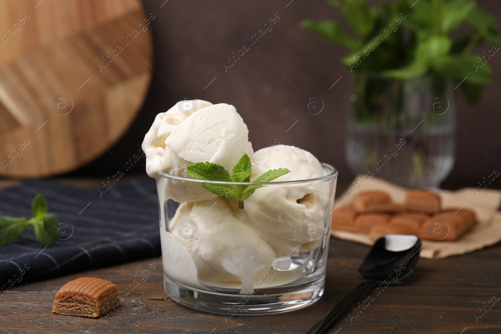 Photo of Scoops of ice cream with mint leaves and caramel candies on wooden table, closeup