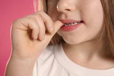 Photo of Little girl biting her nails on pink background, closeup