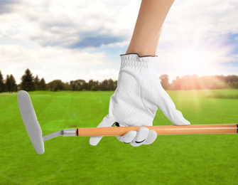 Player holding golf club in park on sunny day, closeup
