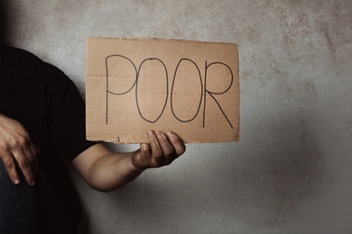 Photo of Man holding carton sign with word POOR on grey background, closeup