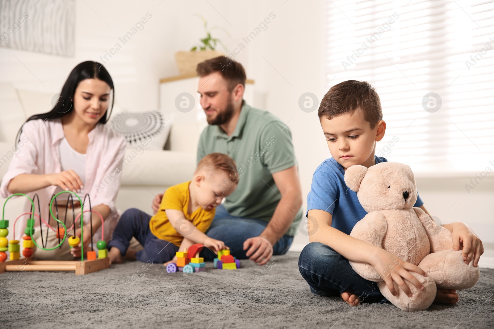 Photo of Unhappy little boy feeling jealous while parents spending time with his baby brother at home