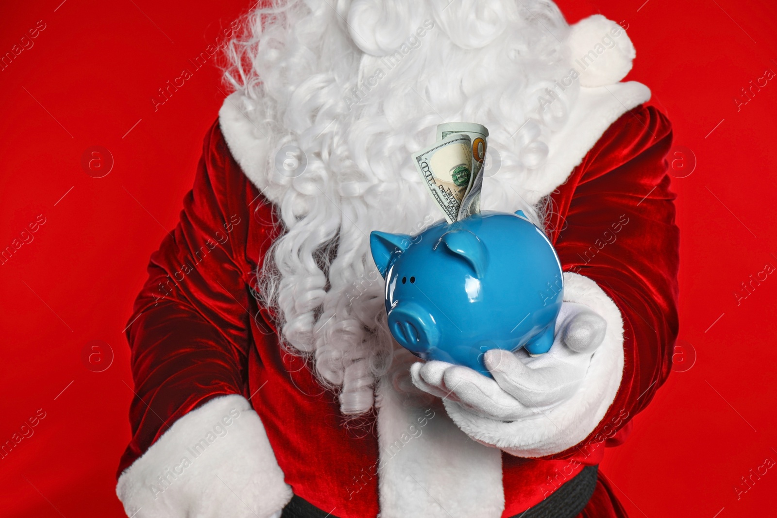 Photo of Santa Claus holding piggy bank with dollar banknotes on red background, closeup
