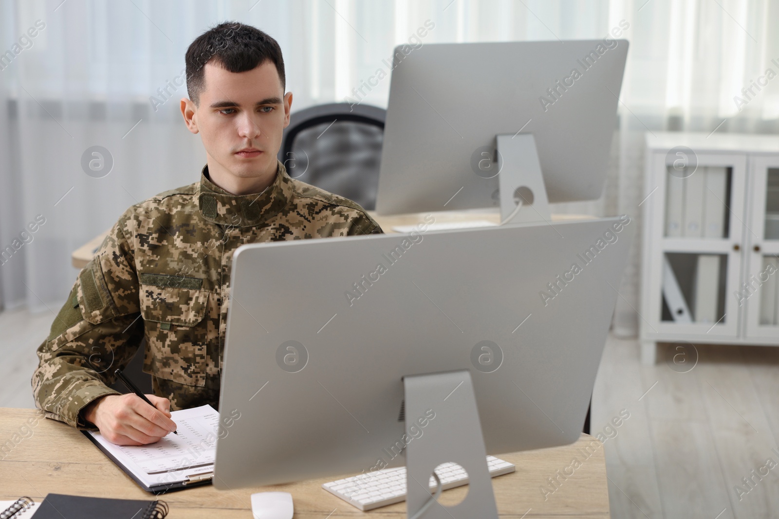 Photo of Military service. Young soldier working at wooden table in office