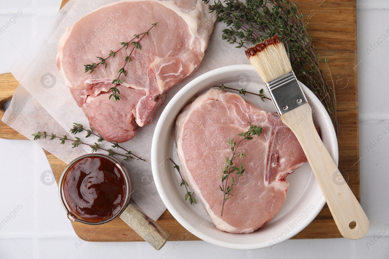 Photo of Raw meat, thyme, basting brush and marinade on white tiled table, top view