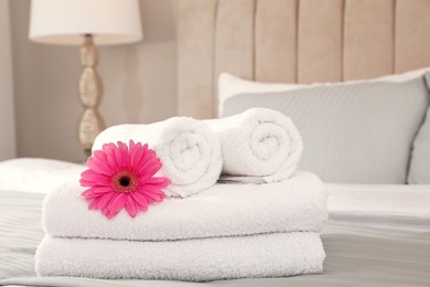Photo of Fresh white towels with flower on bed indoors
