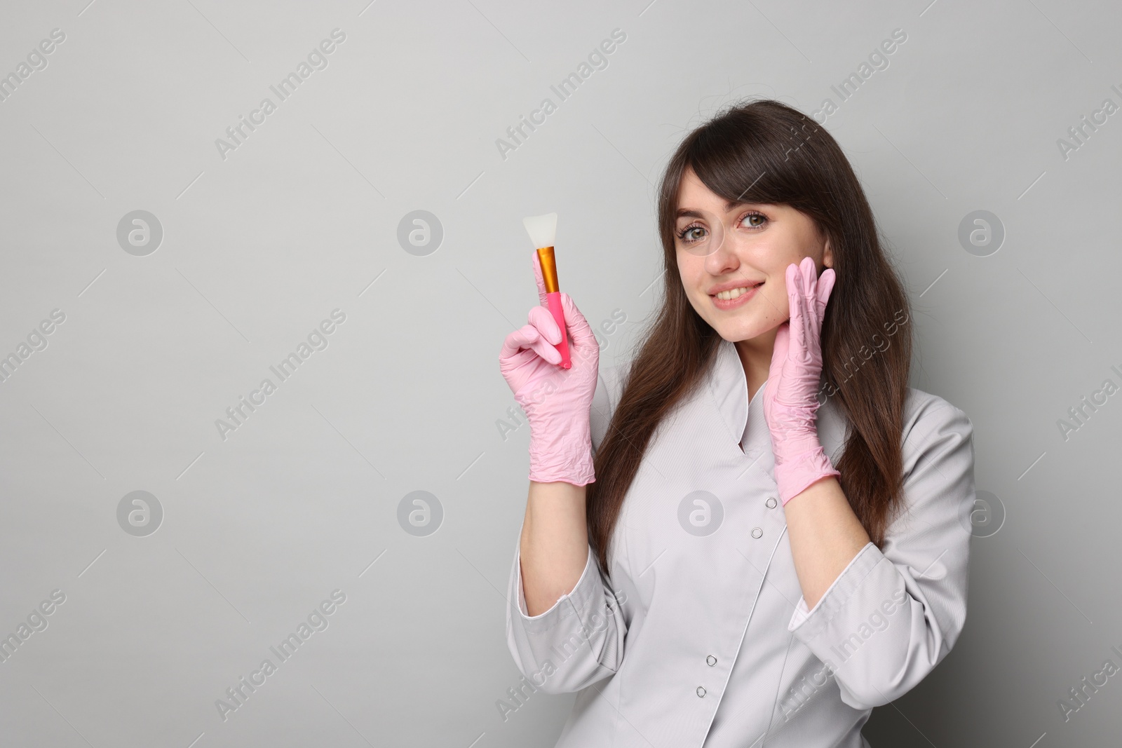 Photo of Cosmetologist with silicone cosmetic brush on grey background, space for text