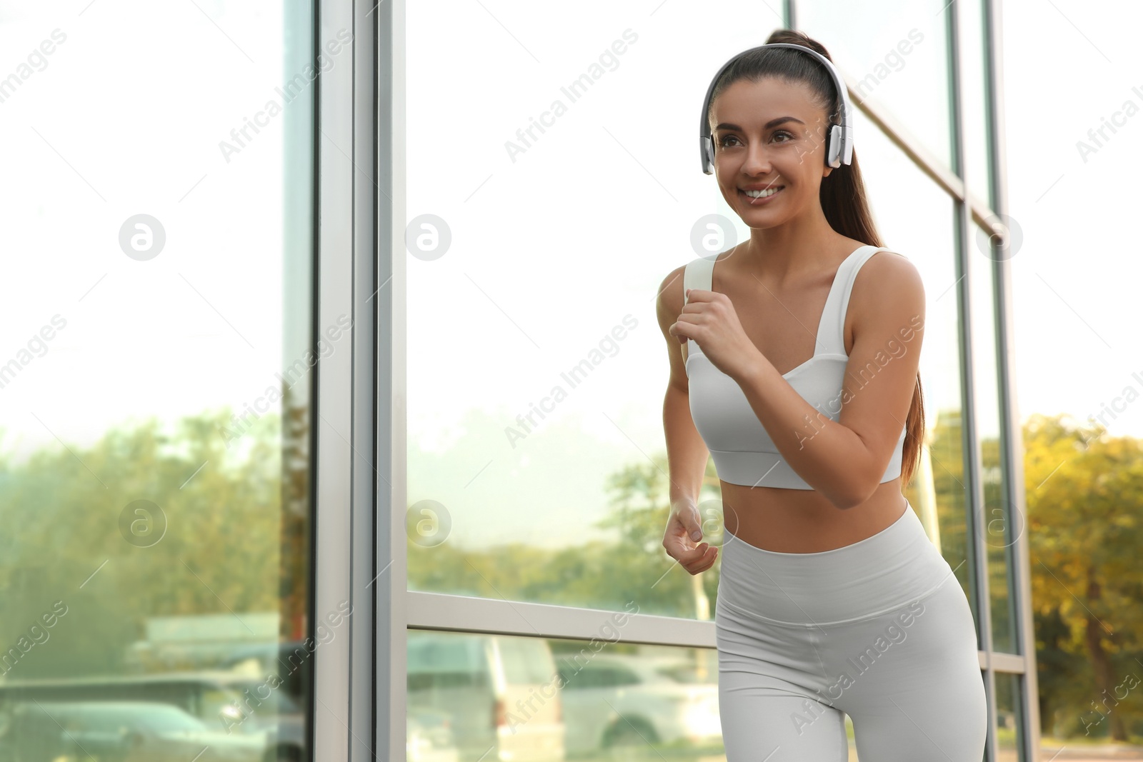 Photo of Young woman in sportswear with headphones running outdoors. Space for text