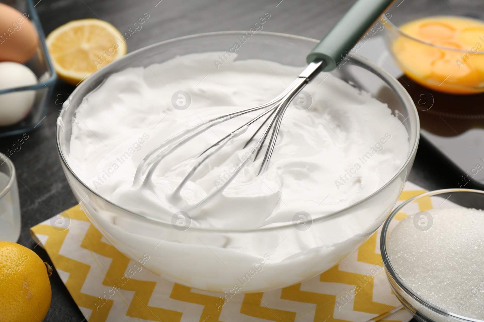 Photo of Bowl with whipped cream, whisk and ingredients on table, closeup