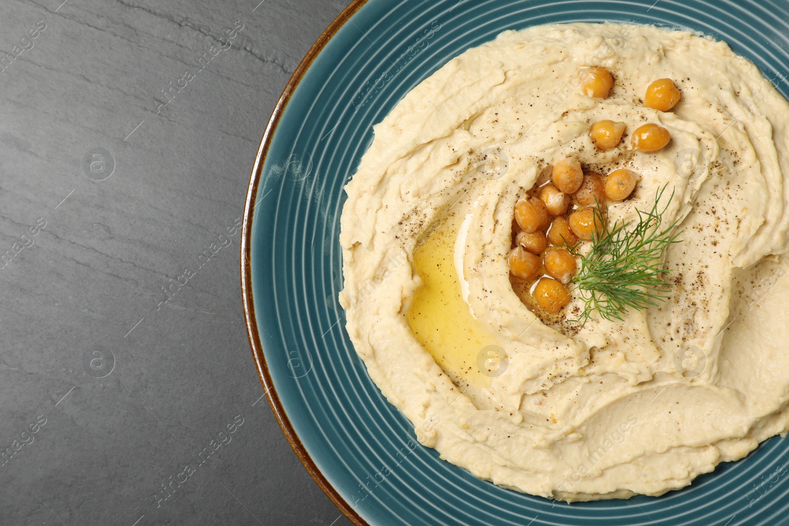 Photo of Plate of tasty hummus with garnish on black table, top view