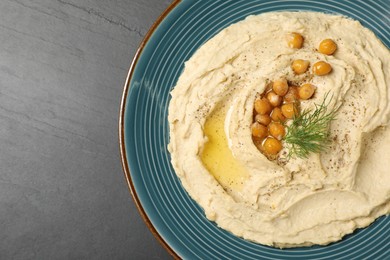 Photo of Plate of tasty hummus with garnish on black table, top view