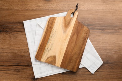 Kitchen towel and cutting board on wooden table, top view