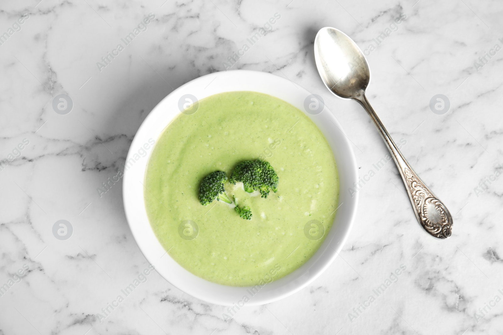 Photo of Delicious broccoli cream soup served on white marble table, flat lay