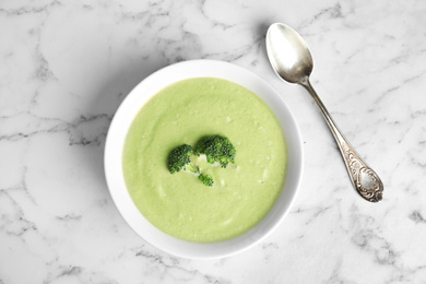 Delicious broccoli cream soup served on white marble table, flat lay