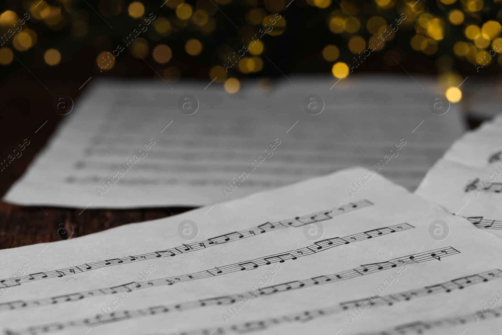 Photo of Closeup view of note sheets on wooden table against blurred lights. Christmas music