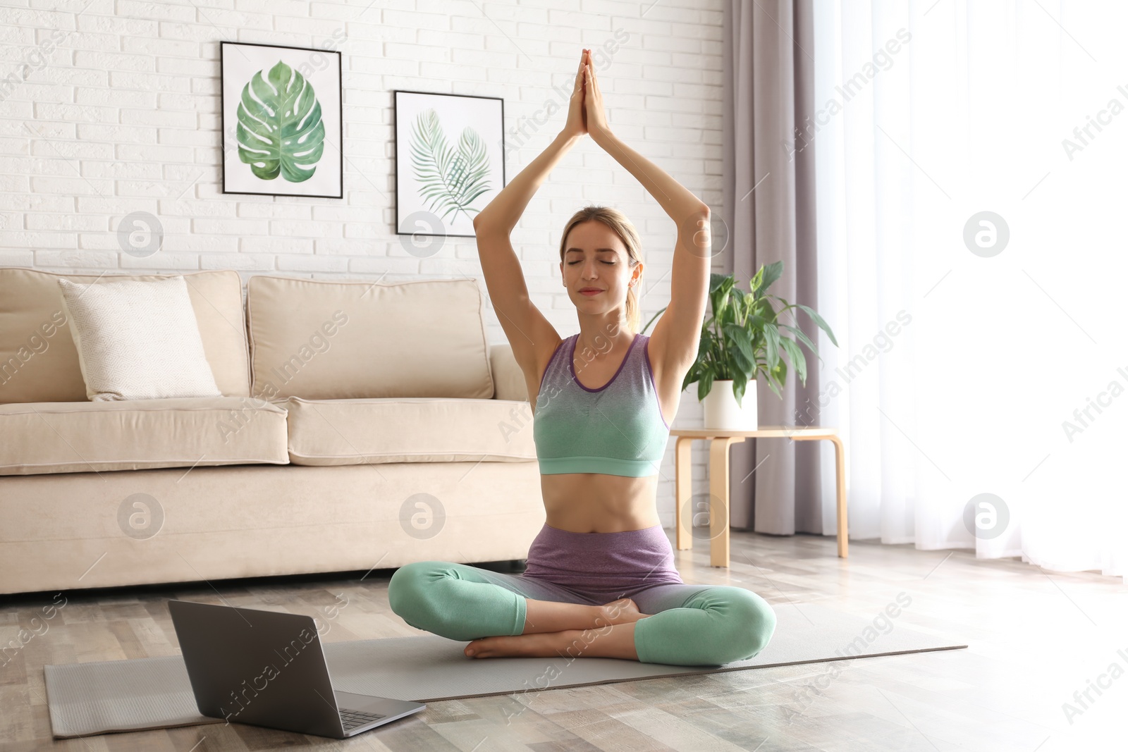 Photo of Woman having online video class via laptop at home. Distance yoga course during coronavirus pandemic