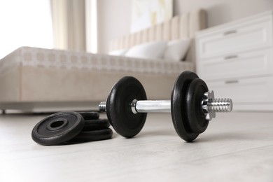 Photo of Steel dumbbell and weight plates on floor indoors. Fitness at home