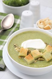Photo of Delicious broccoli cream soup with croutons, sour cream and pumpkin seeds served on white tiled table, closeup
