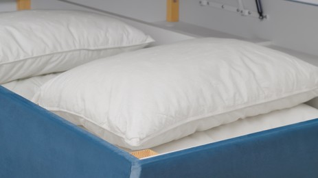 Storage drawer under bed with white pillows indoors, closeup