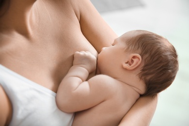 Young woman breastfeeding her baby on blurred background, closeup