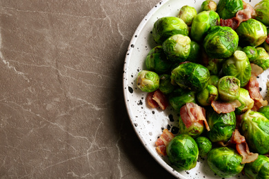 Photo of Delicious Brussels sprouts with bacon on marble table, top view. Space for text