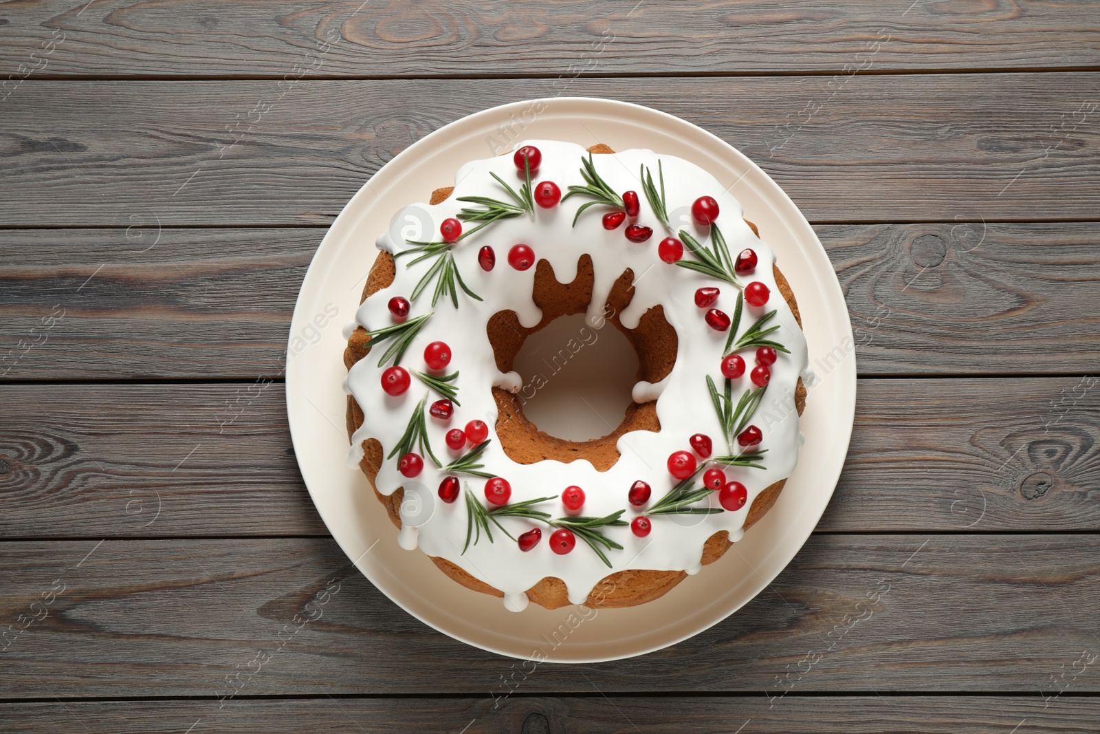 Photo of Traditional Christmas cake decorated with glaze, pomegranate seeds, cranberries and rosemary on wooden table, top view