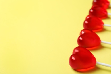 Photo of Sweet heart shaped lollipops on yellow background, closeup view with space for text. Valentine's day celebration