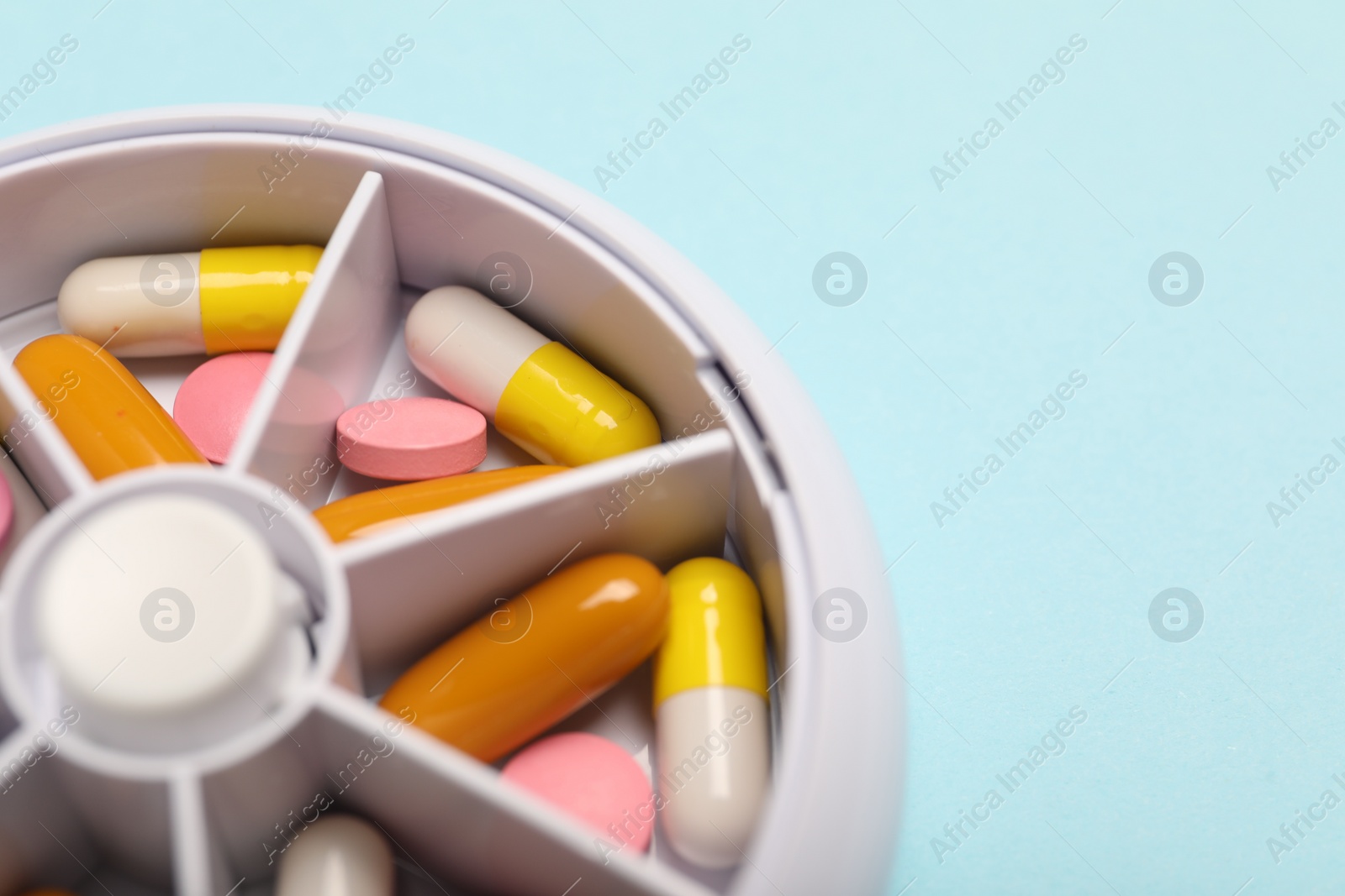 Photo of Different pills in organizer on light blue background, closeup. Space for text