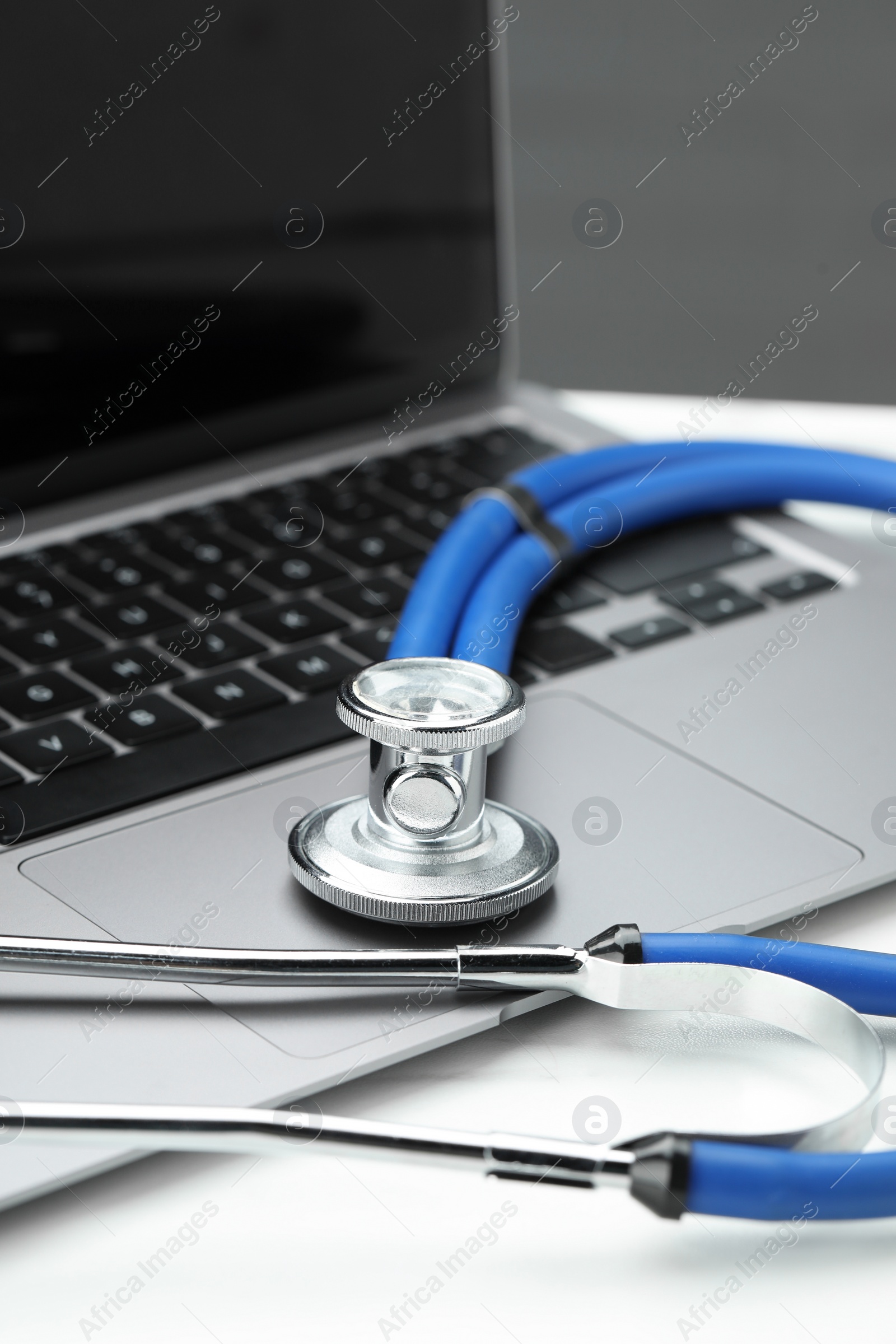 Photo of Stethoscope and modern laptop on white table, closeup