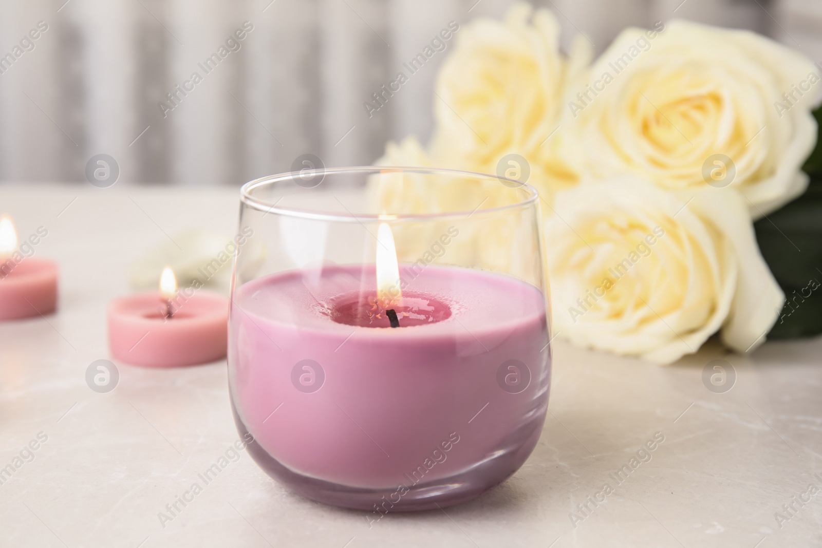 Photo of Burning candle in glass holder and roses on light table