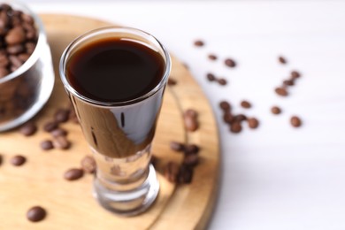 Photo of Shot glass of coffee liqueur and beans on white table, closeup. Space for text