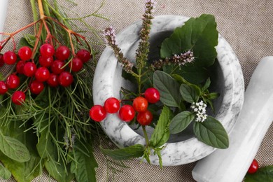 Photo of Marble mortar with different herbs, berries and pestle on cloth, top view