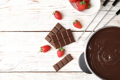 Flat lay composition with chocolate fondue in pot and space for text on wooden background