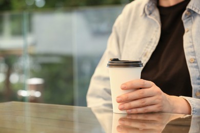 Woman holding takeaway paper cup at table, closeup and space for text. Coffee to go