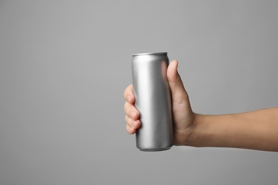 Woman holding aluminum can with beverage on grey background, closeup. Space for design