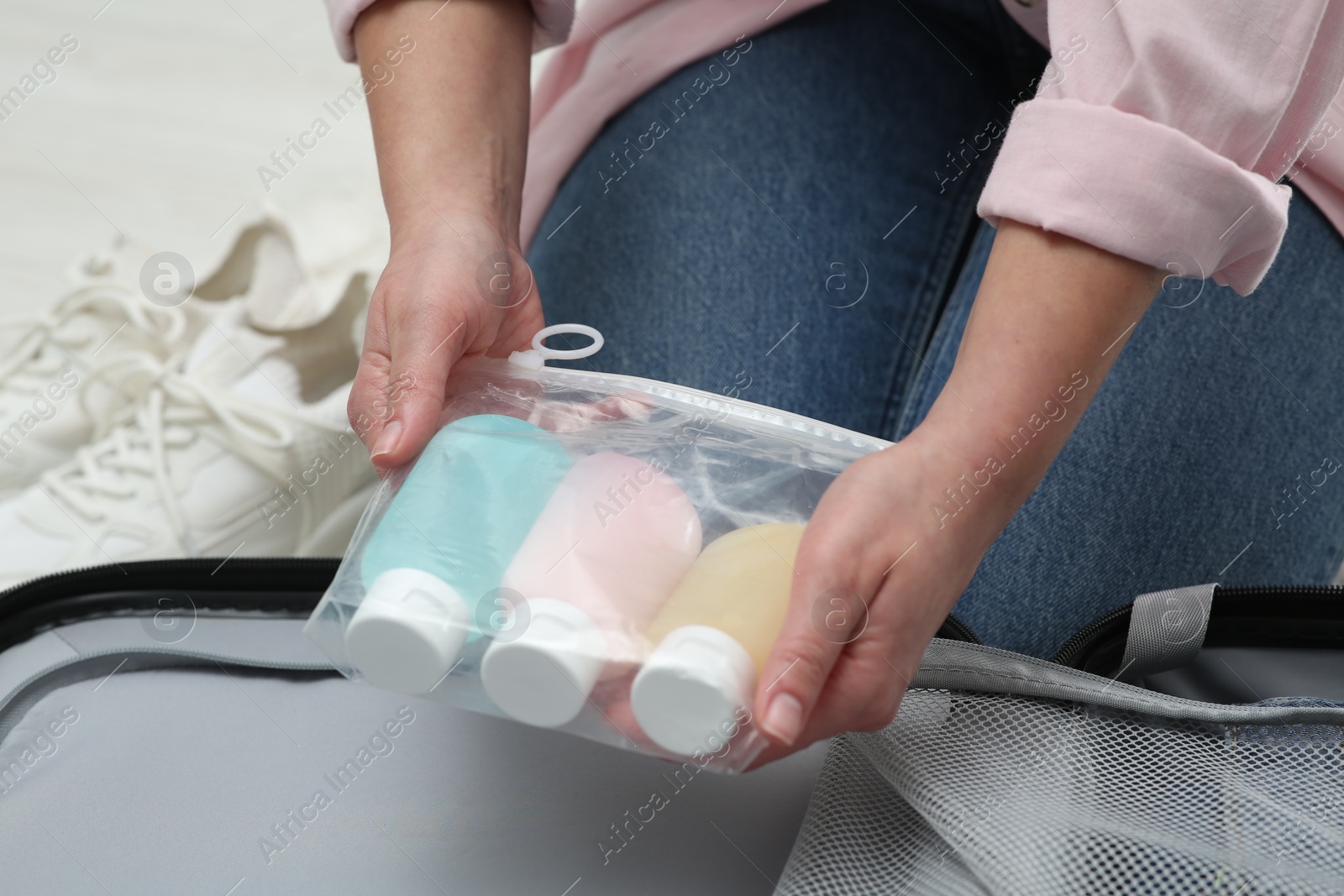 Photo of Woman with plastic bag of cosmetic travel kit packing suitcase, closeup. Bath accessories