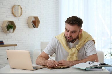Photo of Young man taking notes during online webinar at table indoors