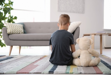 Photo of Lonely little boy with teddy bear sitting on floor at home. Autism concept