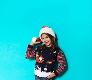 Photo of Cute little girl in Christmas sweater and hat on color background