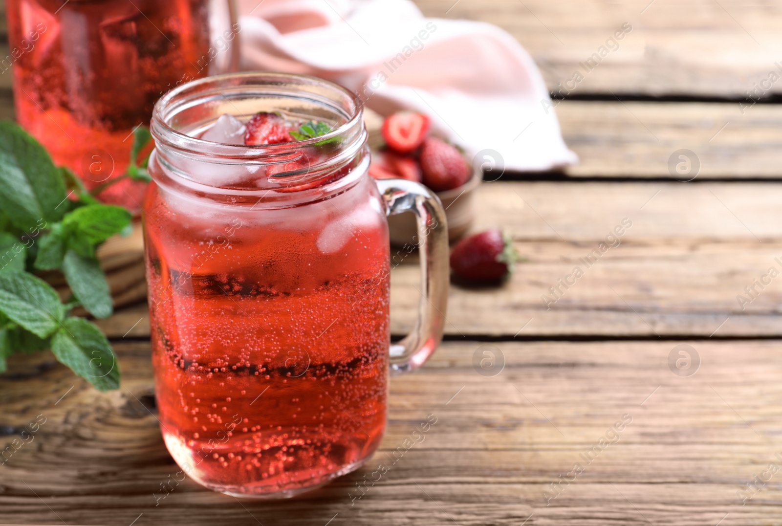 Photo of Delicious strawberry lemonade made with soda water and fresh ingredients on wooden table. Space for text