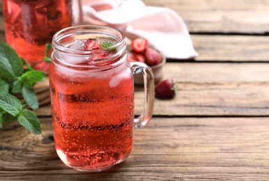 Photo of Delicious strawberry lemonade made with soda water and fresh ingredients on wooden table. Space for text