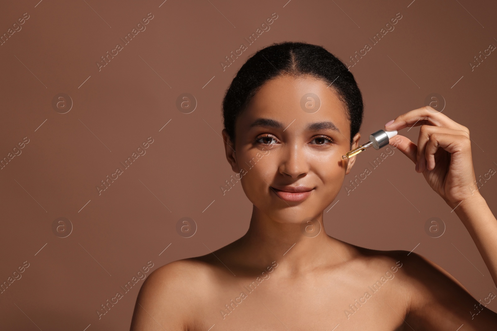 Photo of Beautiful woman applying serum onto her face on brown background. Space for text
