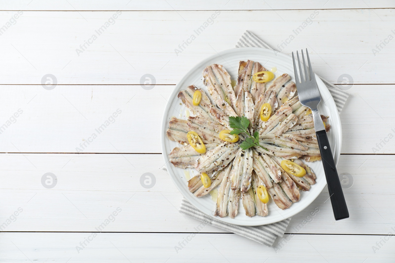 Photo of Tasty pickled anchovies with spices and fork on white wooden table, top view. Space for text