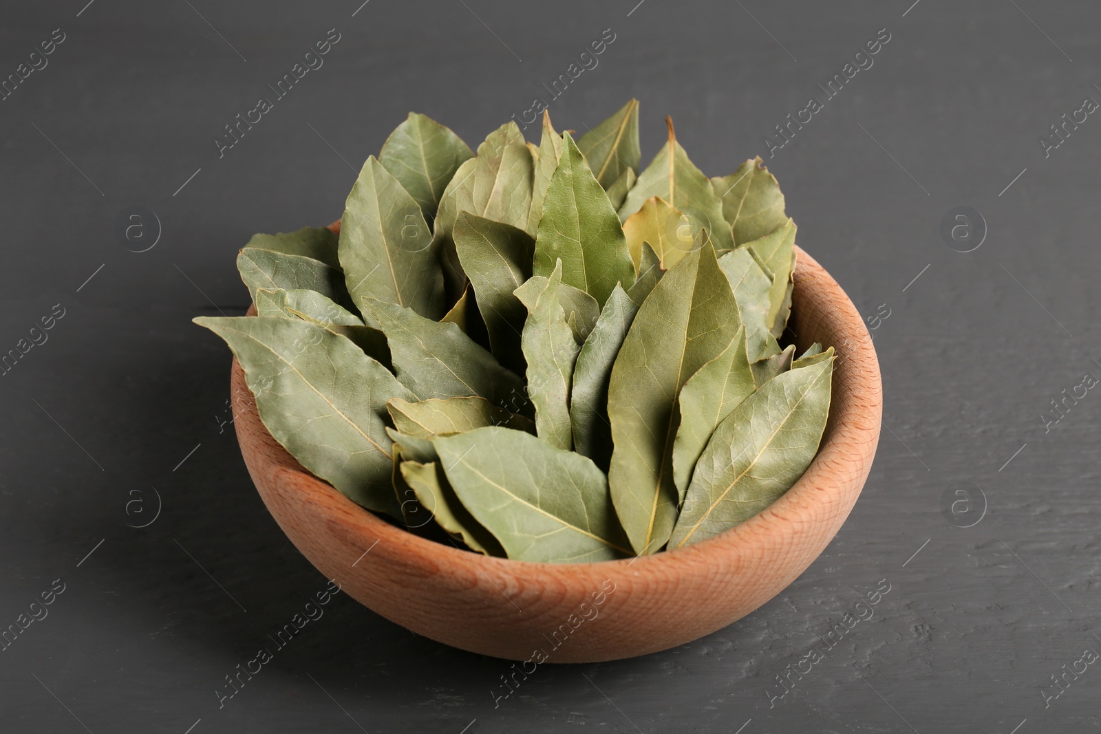 Photo of Aromatic bay leaves in wooden bowl on gray table