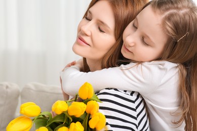 Mother and her cute daughter with bouquet of yellow tulips at home