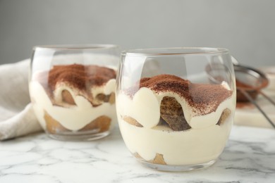 Photo of Delicious tiramisu in glasses on white marble table, closeup