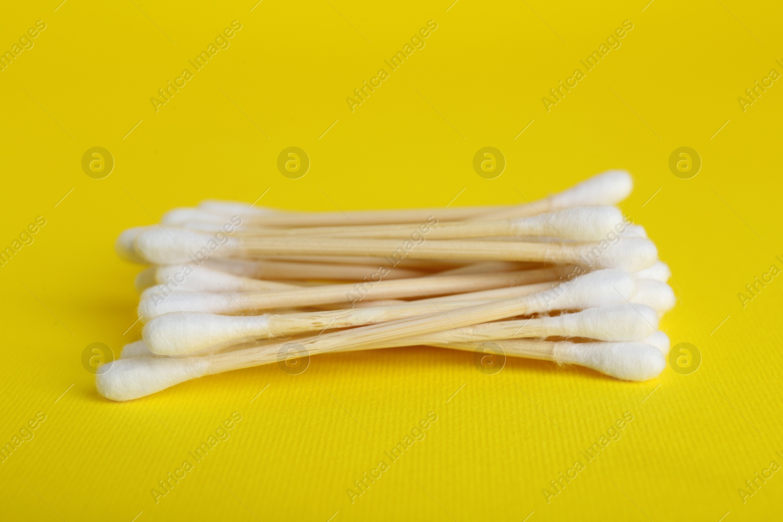 Photo of Wooden cotton buds on yellow background, closeup