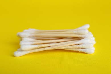 Photo of Wooden cotton buds on yellow background, closeup