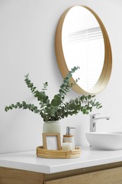 Photo of Vase with eucalyptus branches and toiletries near vessel sink in bathroom. Interior design