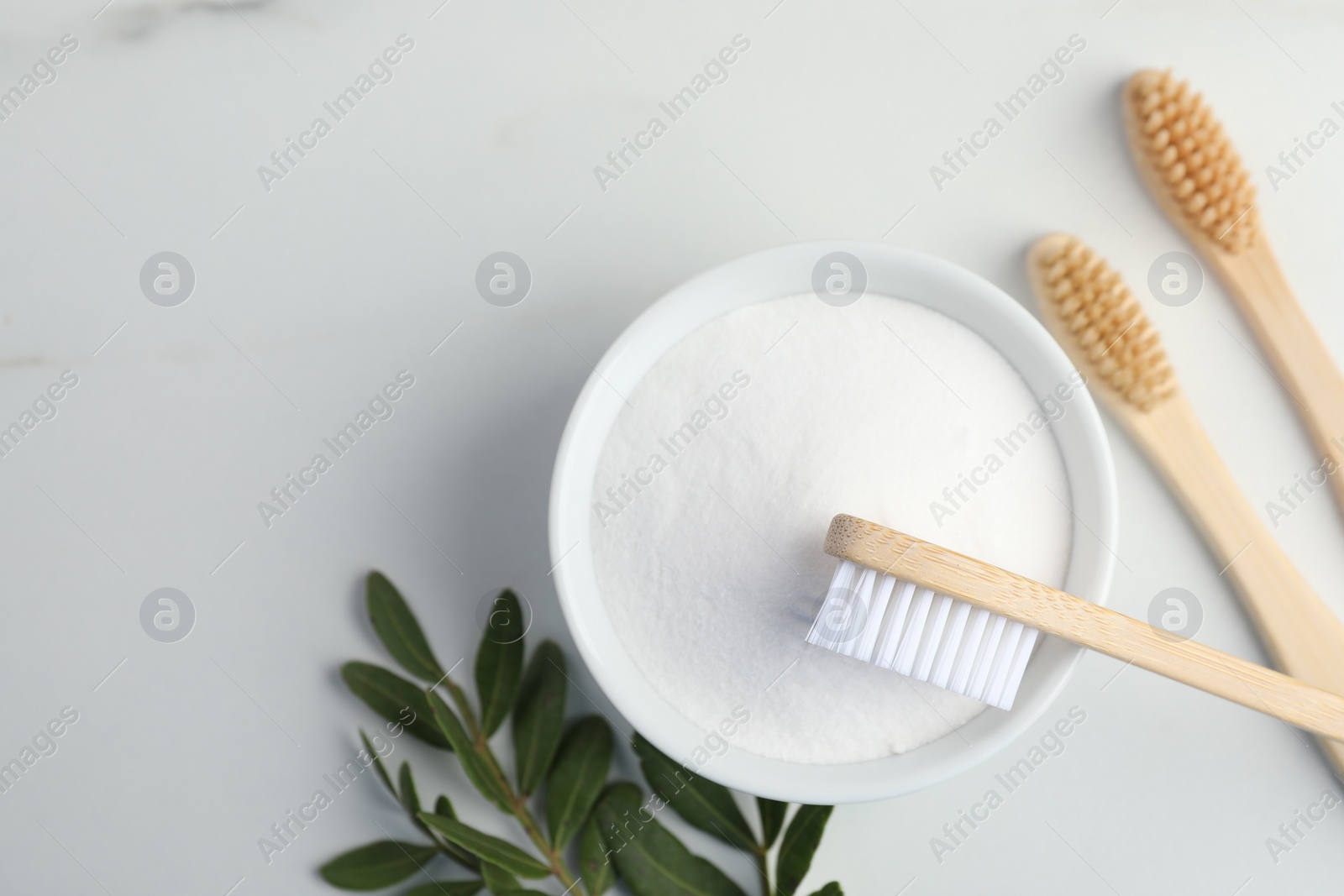 Photo of Bamboo toothbrushes, bowl of baking soda and green leaves on white marble table, flat lay. Space for text